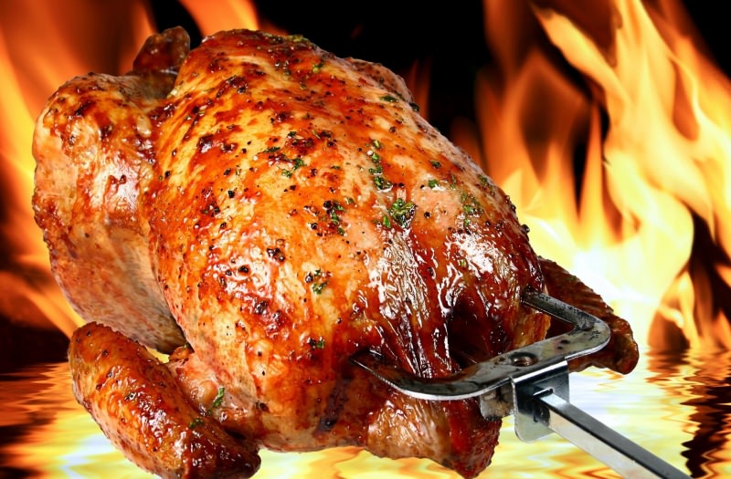 Cottura di un pollo allo spiedo con girarrosto su barbecue a gas e carbone.